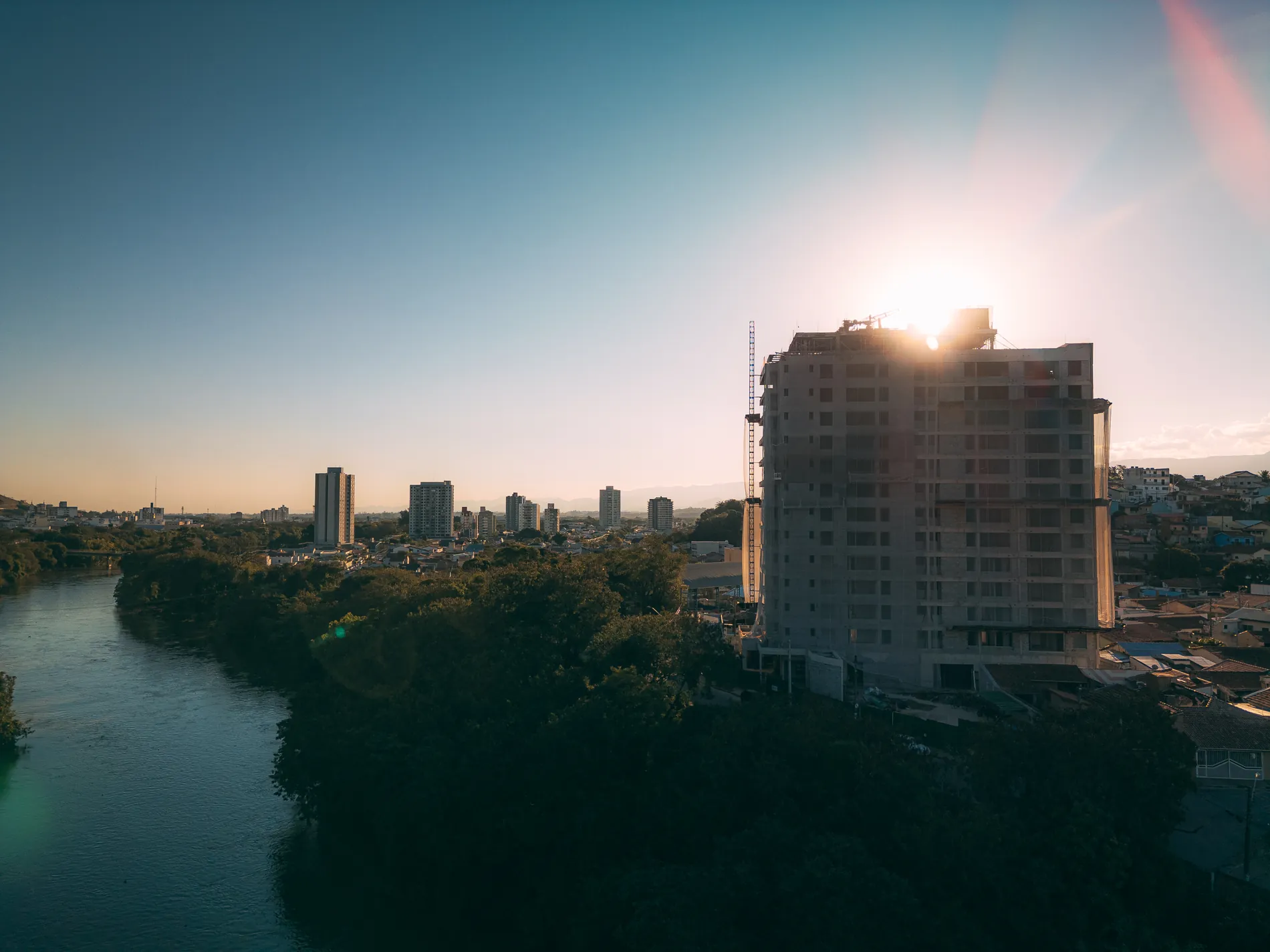 Torre do Ápice em construção ao entardecer, com o rio Paraíba do Sul à esquerda e sol se pondo ao fundo, em Guaratinguetá